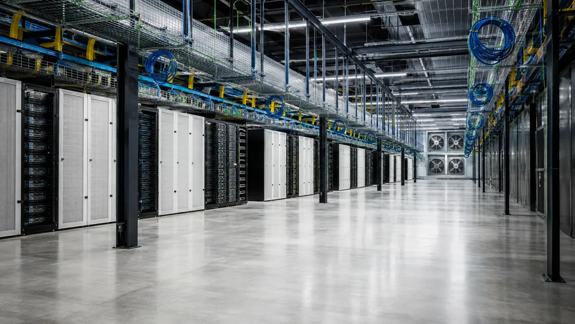 Illustration. A data hall aisle with white containment panels and cabinet doors along one side, cable tray and coiled cable overhead, and a bank of fan-wall units at the far end.